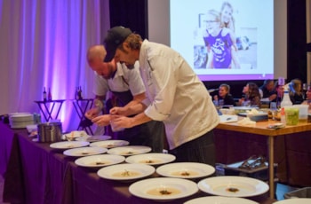Two chefs plating meals for several guest